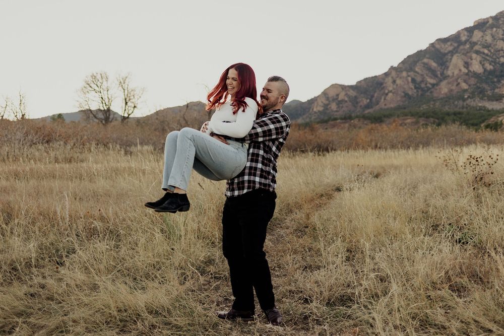 A couple dancing and laughing together in a sunlit meadow with mountains in the distance.