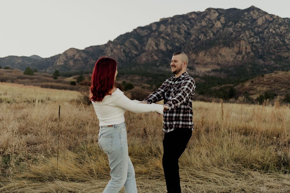 Happy couple embracing and laughing in an autumn field with scenic mountains in the distance.