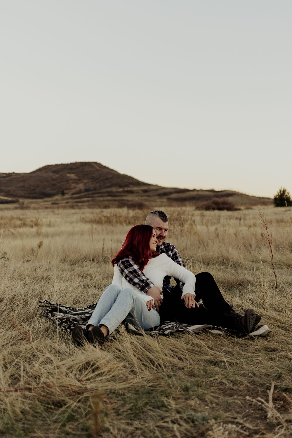 A couple relaxing together on a blanket in a grassy field during sunset.