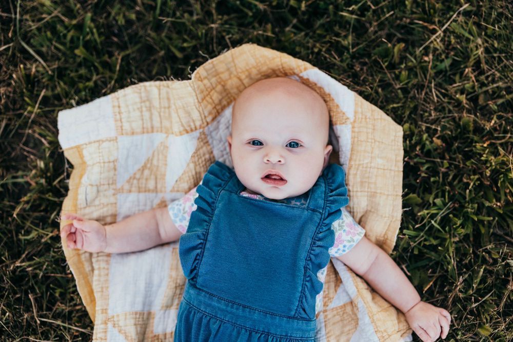A series of images shows a baby wearing a denim outfit laying on a white blanket outdoors against green grass.