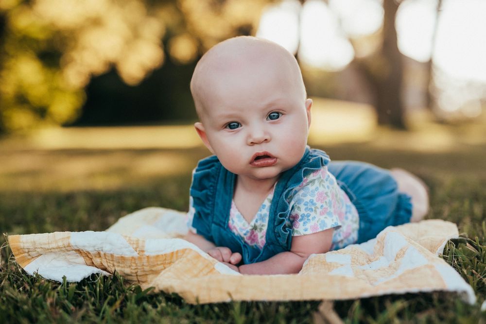 Baby wearing blue shirt lies on cream blanket outdoors during golden hour photoshoot.