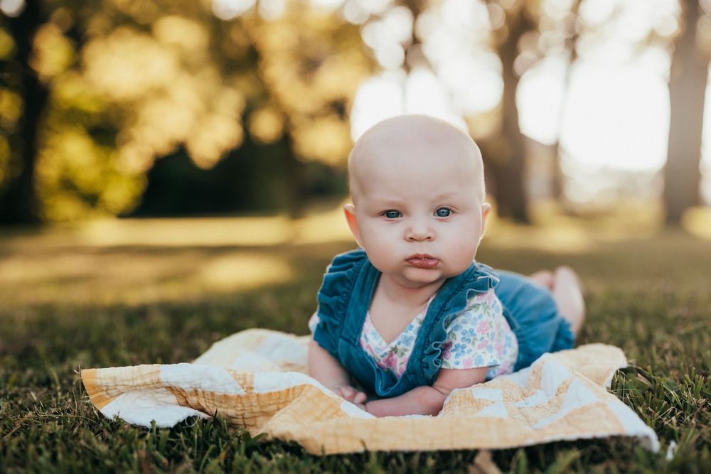 A child in a floral patterned outfit lies on colorful star-print blanket outdoors during a sunny day.