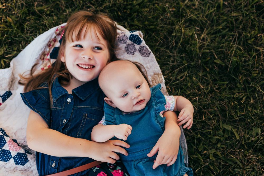 Three children lie together on grass during autumn while laughing and playing outdoors.
