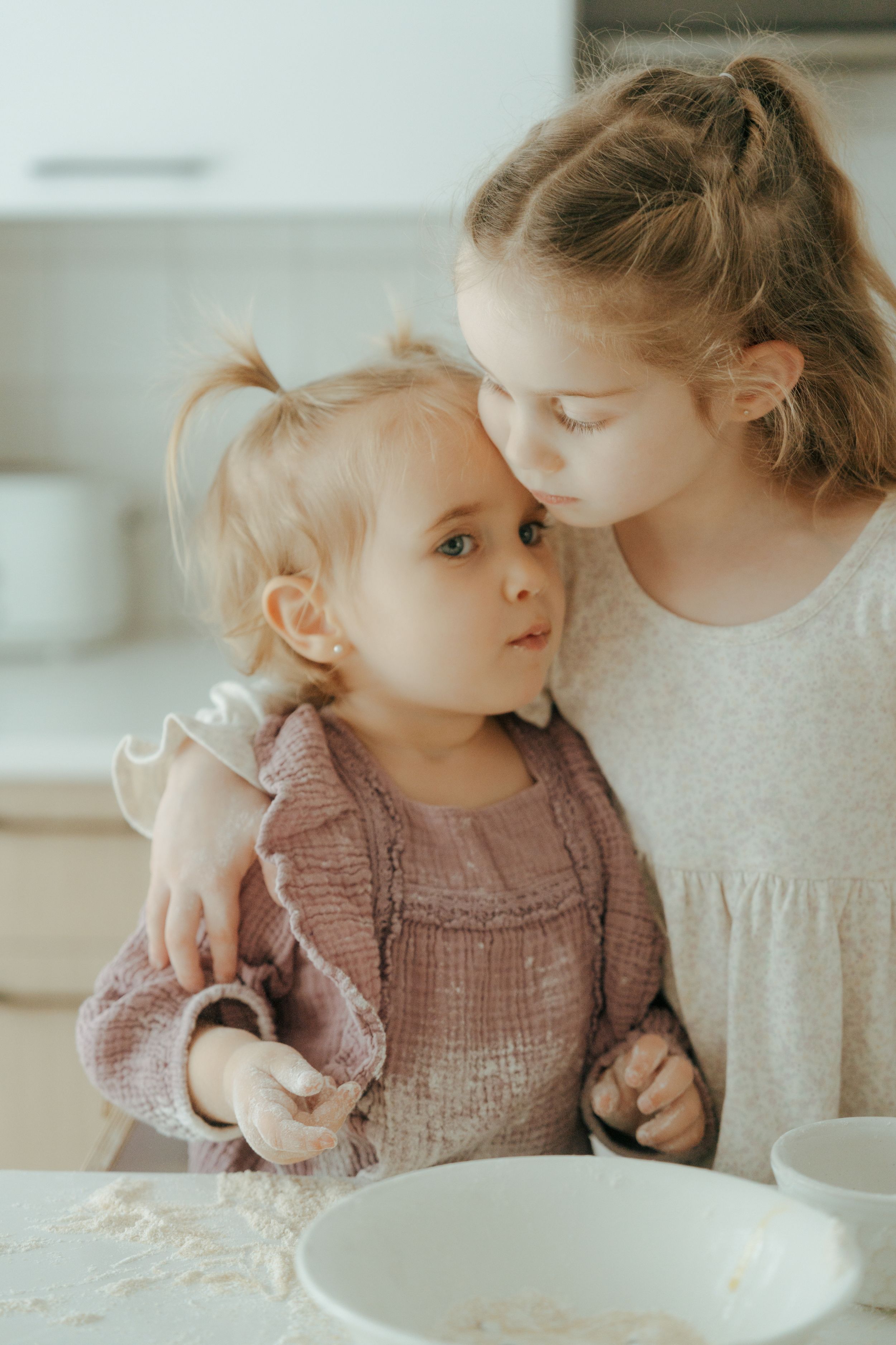 Two people in soft neutral tones stare intently at a mixing bowl while baking together in a bright kitchen.