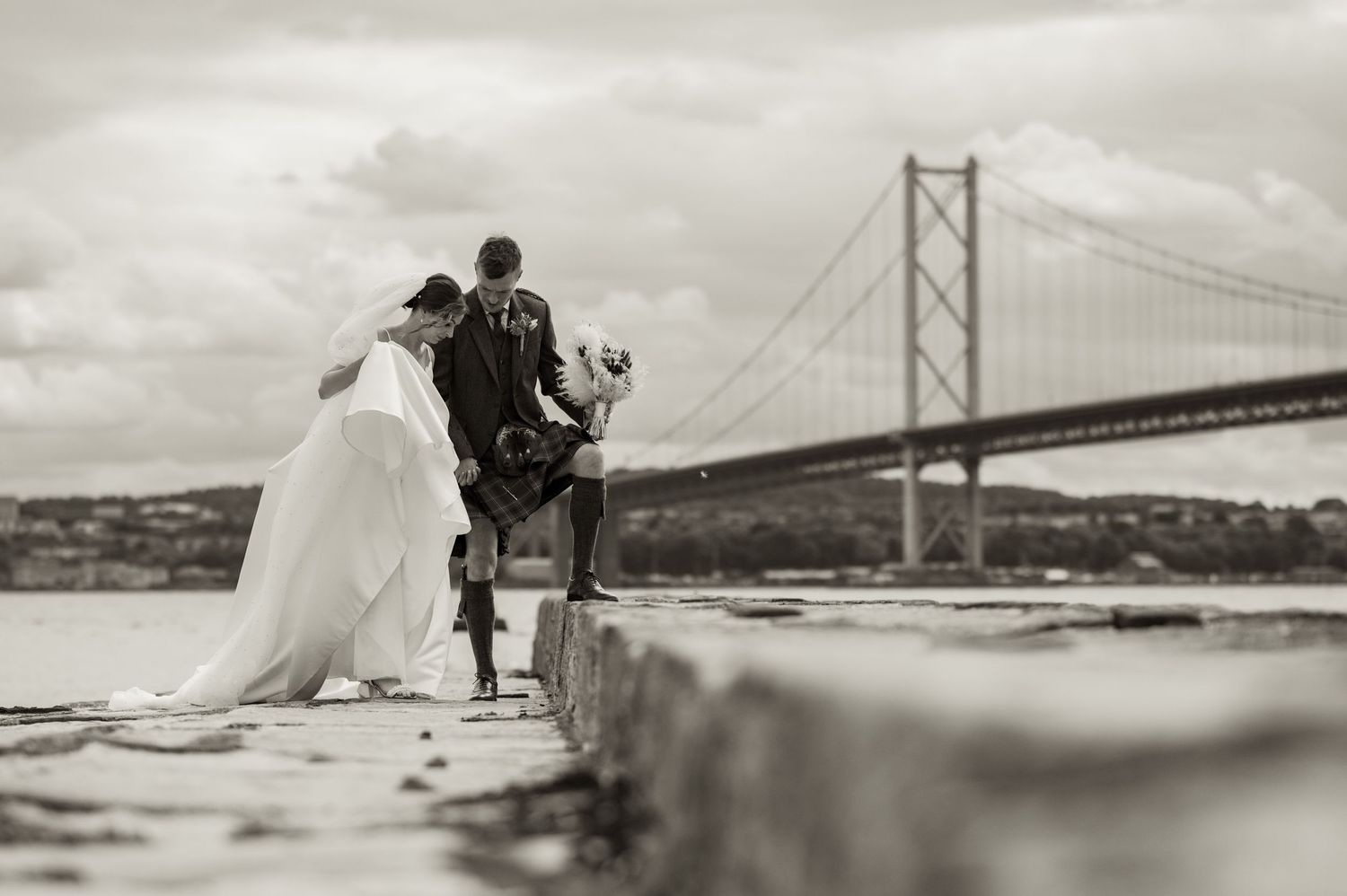 A couple in wedding attire poses under the iconic Golden Gate Bridge in San Francisco during a romantic photo session.