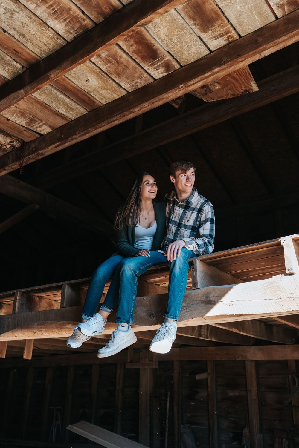 Couple sitting on wooden beams in a rustic barn attic.