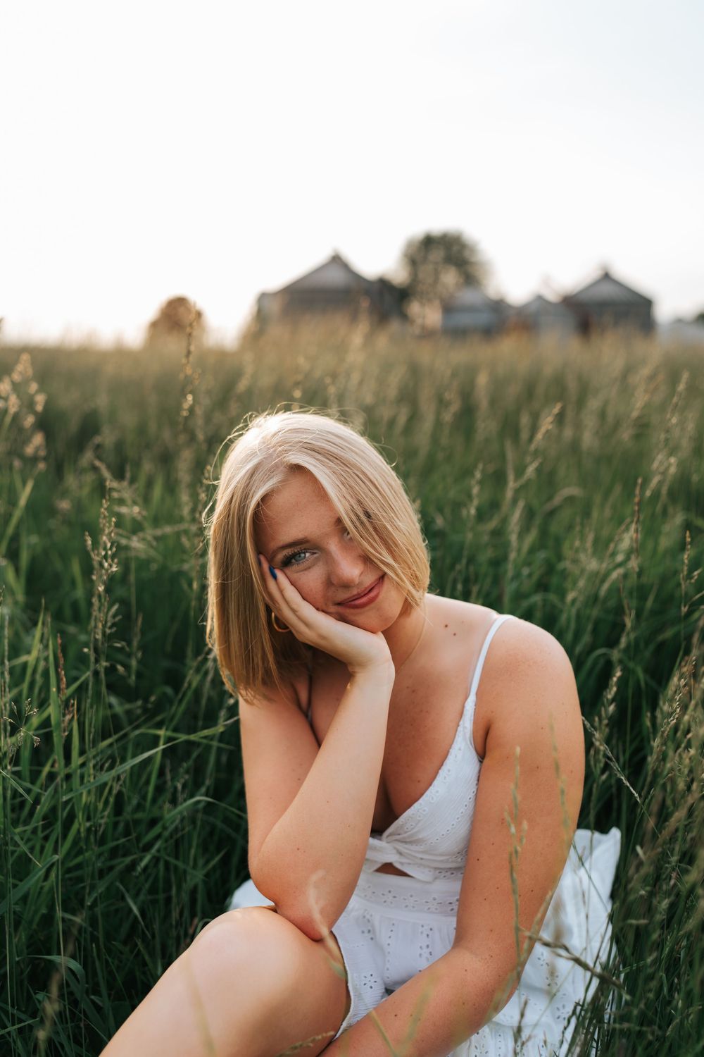 Person in white dress sitting peacefully in a tall grass field.