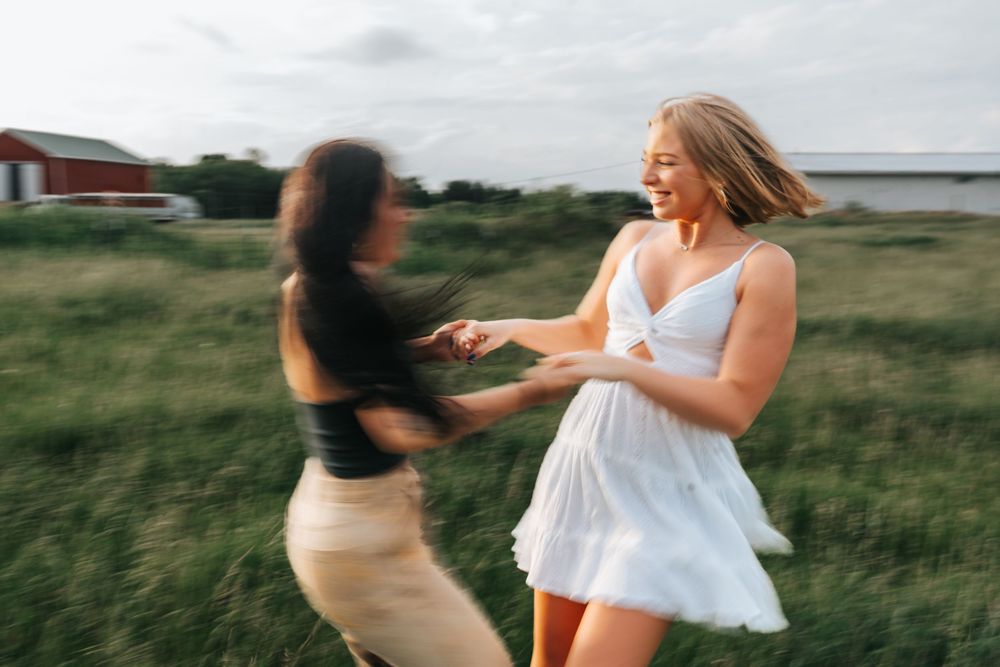 Two people dancing and spinning joyfully in a grassy field at sunset.