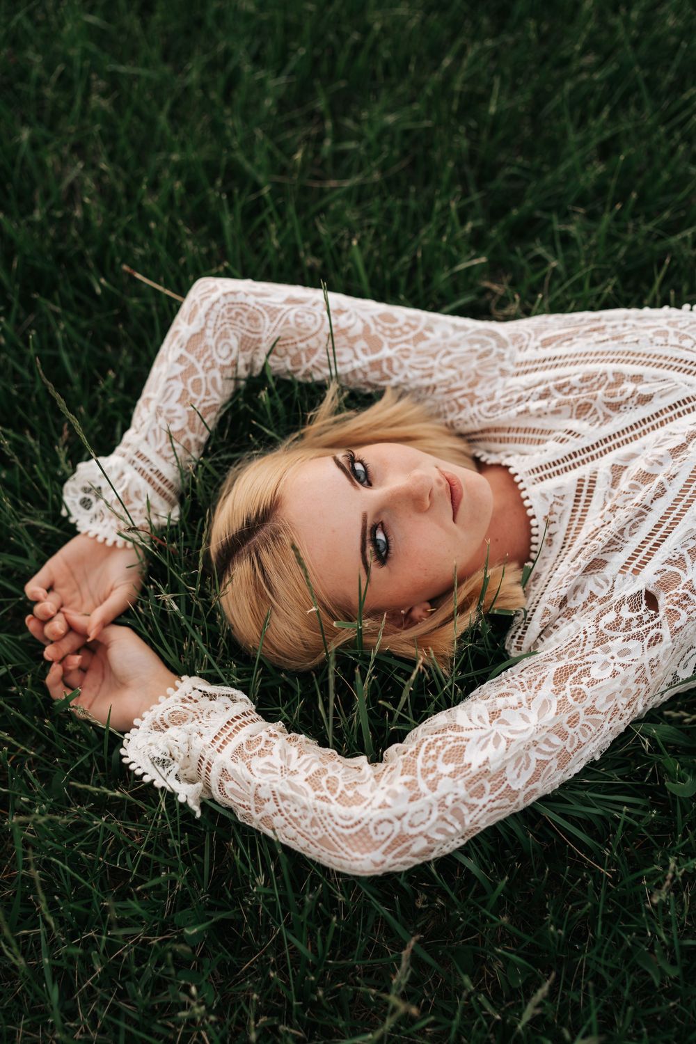 Woman in delicate lace dress lying in green grass.