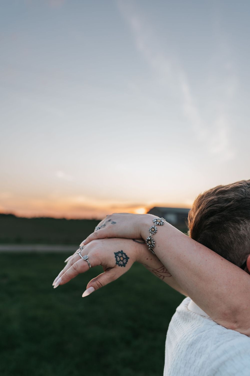 Hand with detailed tattoos and rings against a sunset sky.