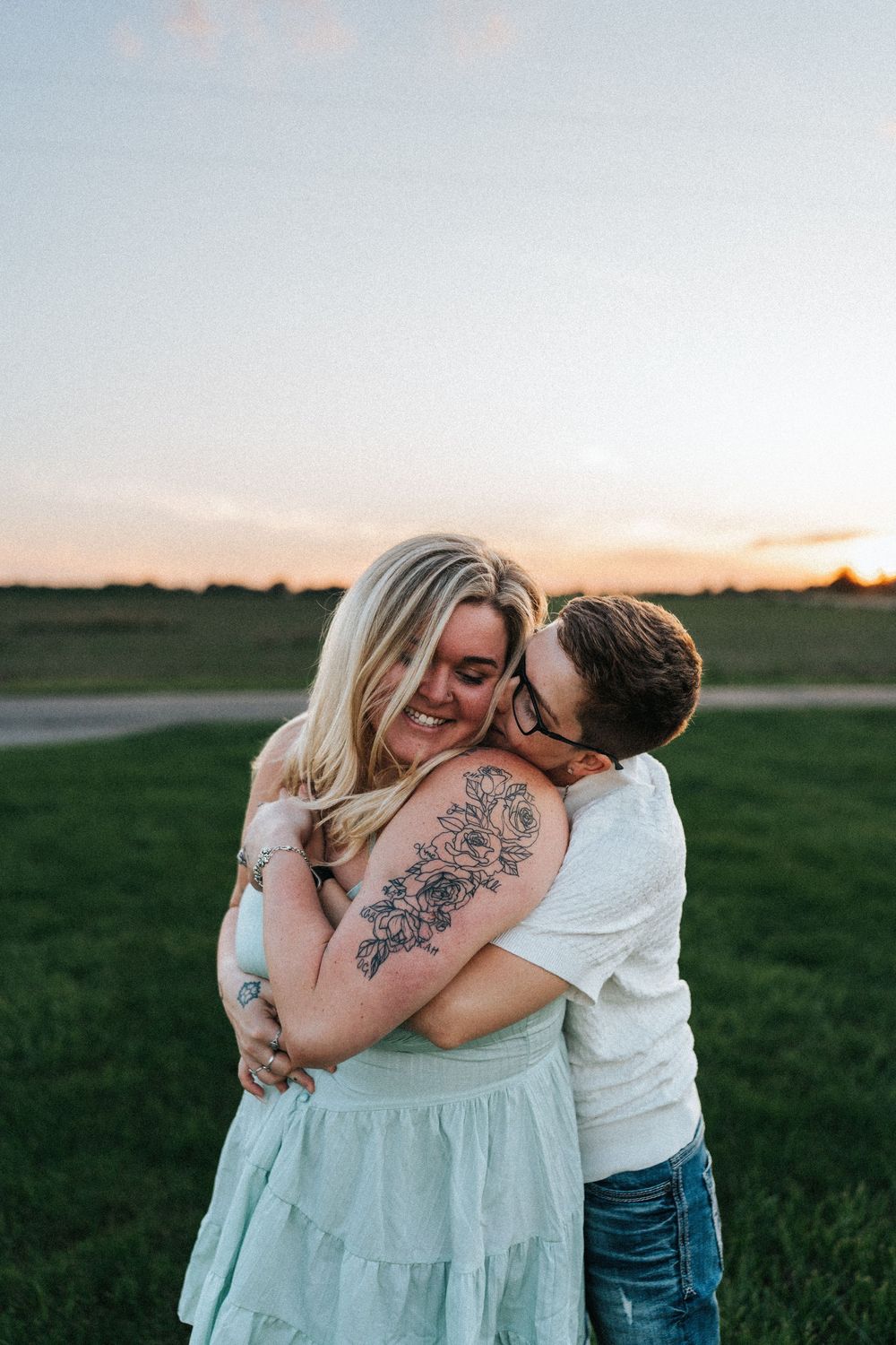 Intimate embrace between couple in white clothing during golden hour in a field.