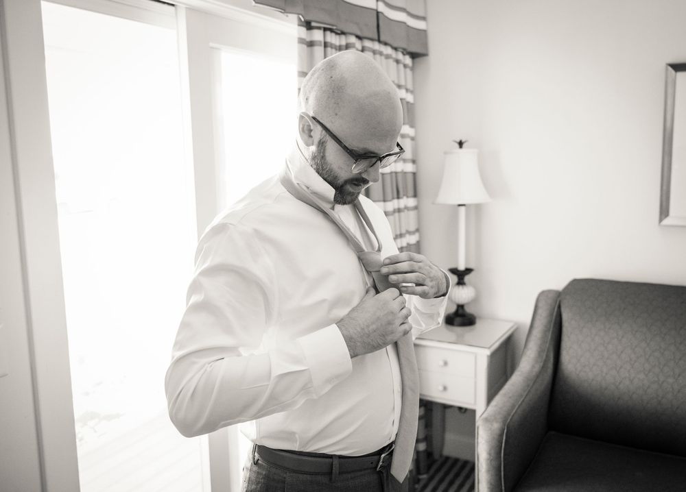 A person adjusting their tie while getting ready in a bright room with white decor.