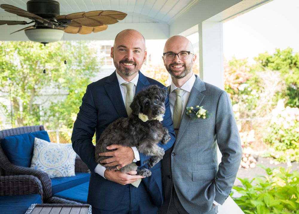 Wedding party posing outdoors on a porch with a fluffy black dog.