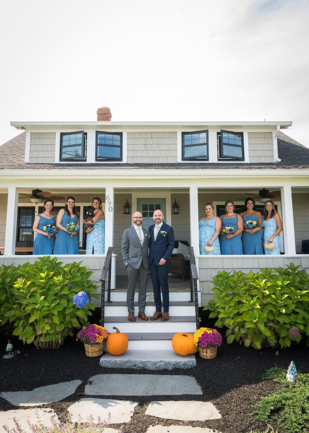 Wedding party poses on the front porch of a coastal home decorated with fall pumpkins and blue accents.