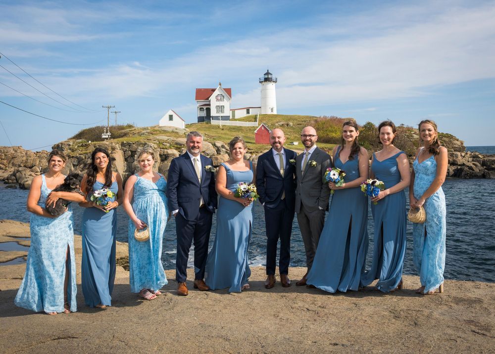 Wedding party poses for photo at Nubble Lighthouse in Maine with blue bridesmaid dresses.