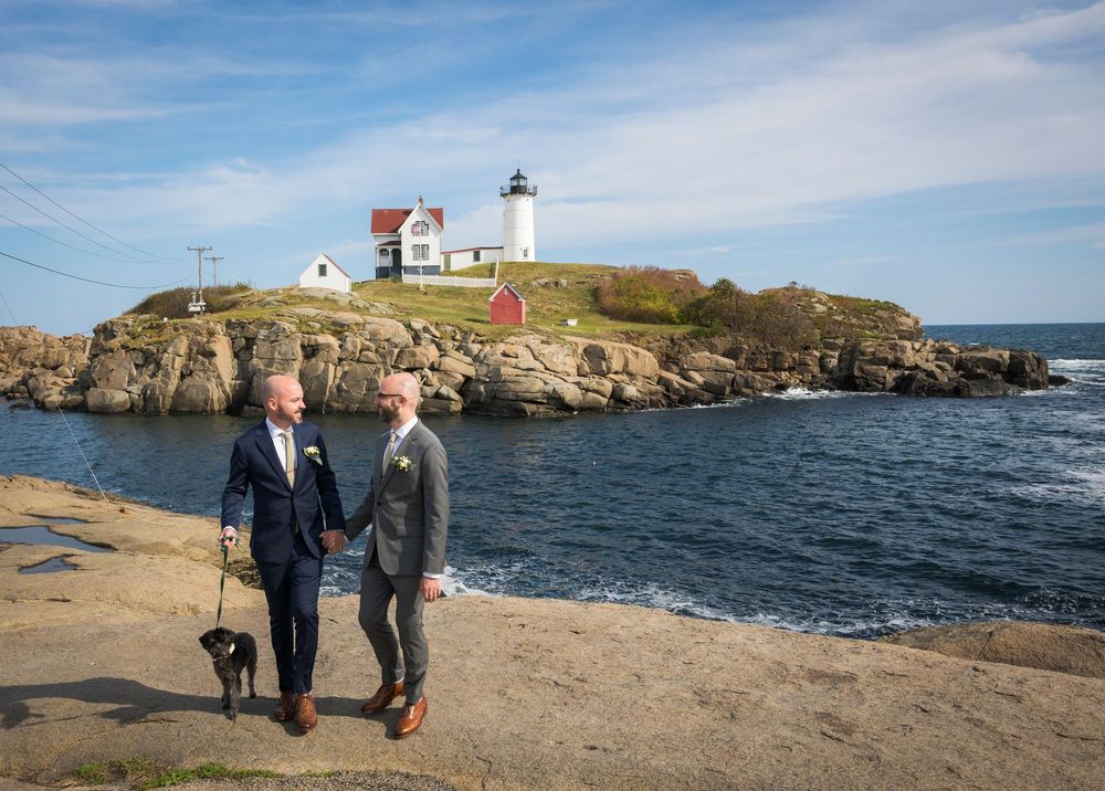 Couple walking with dog near Nubble Lighthouse in Maine on a sunny day.