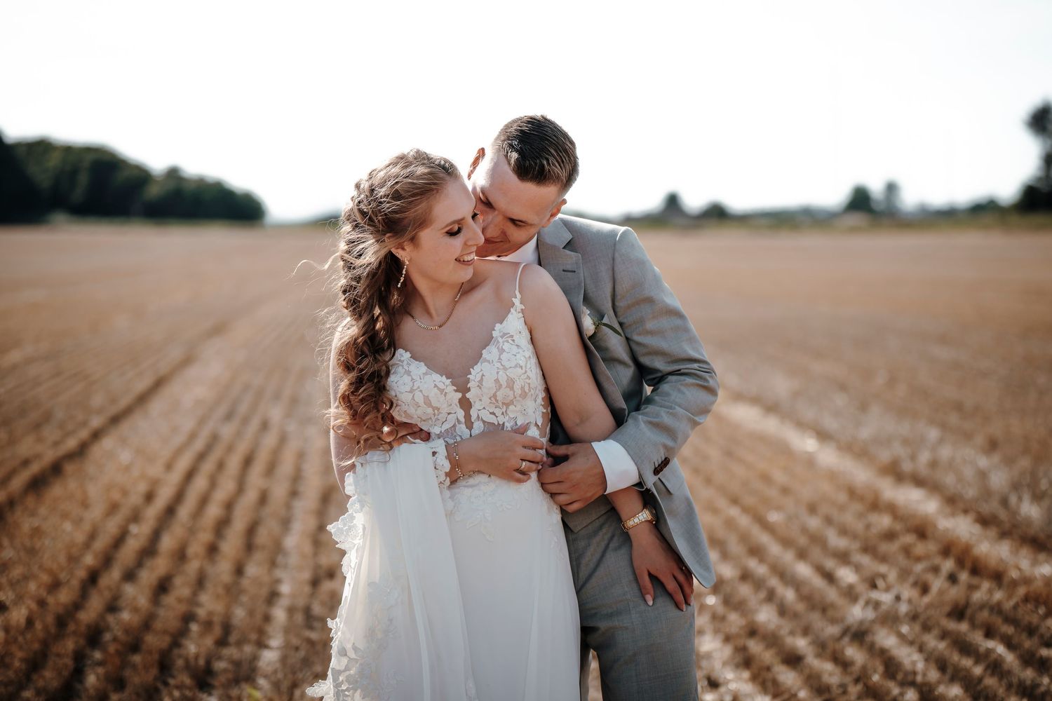 A romantic wedding couple embraces in a golden harvested wheat field during sunset.