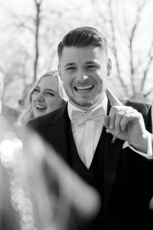 Groomsmen in black tuxedos and white ties share laughter during wedding photos outdoors.