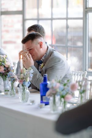 Emotional moments captured at decorated wedding reception table with brick wall backdrop.