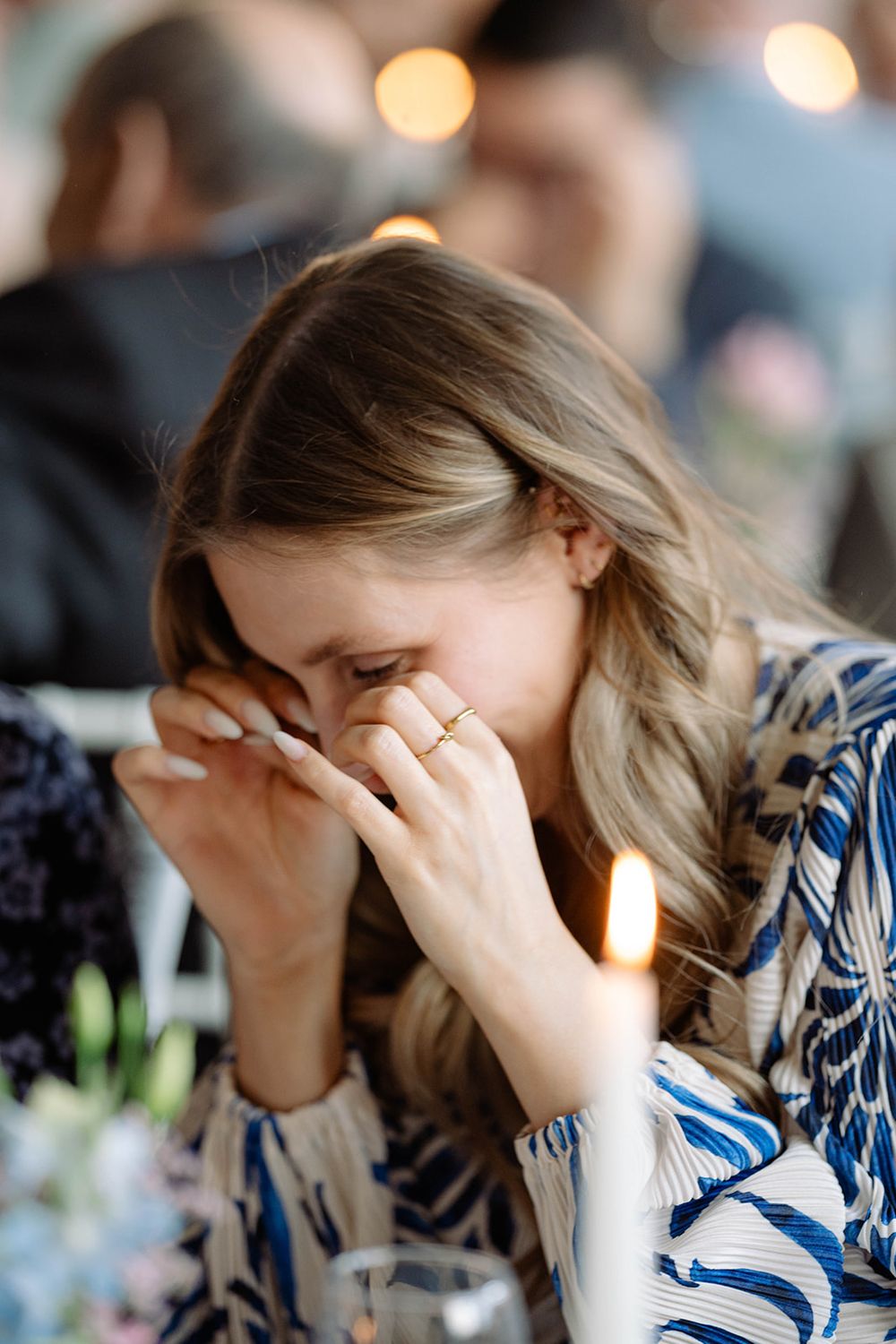 Wedding guest shows emotional response during reception with soft lighting and table settings.