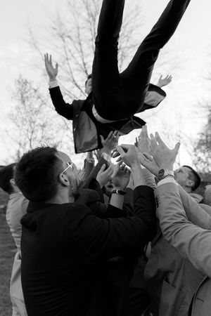 Black and white photo of a person being tossed in the air during a celebratory group moment.