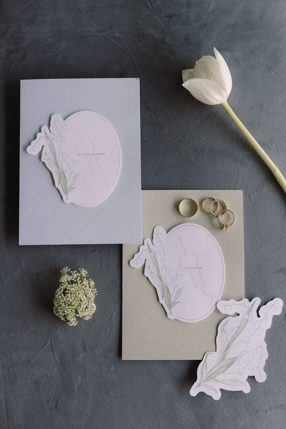 Minimalist white embossed wedding stationery with floral accents and rings on dark background.