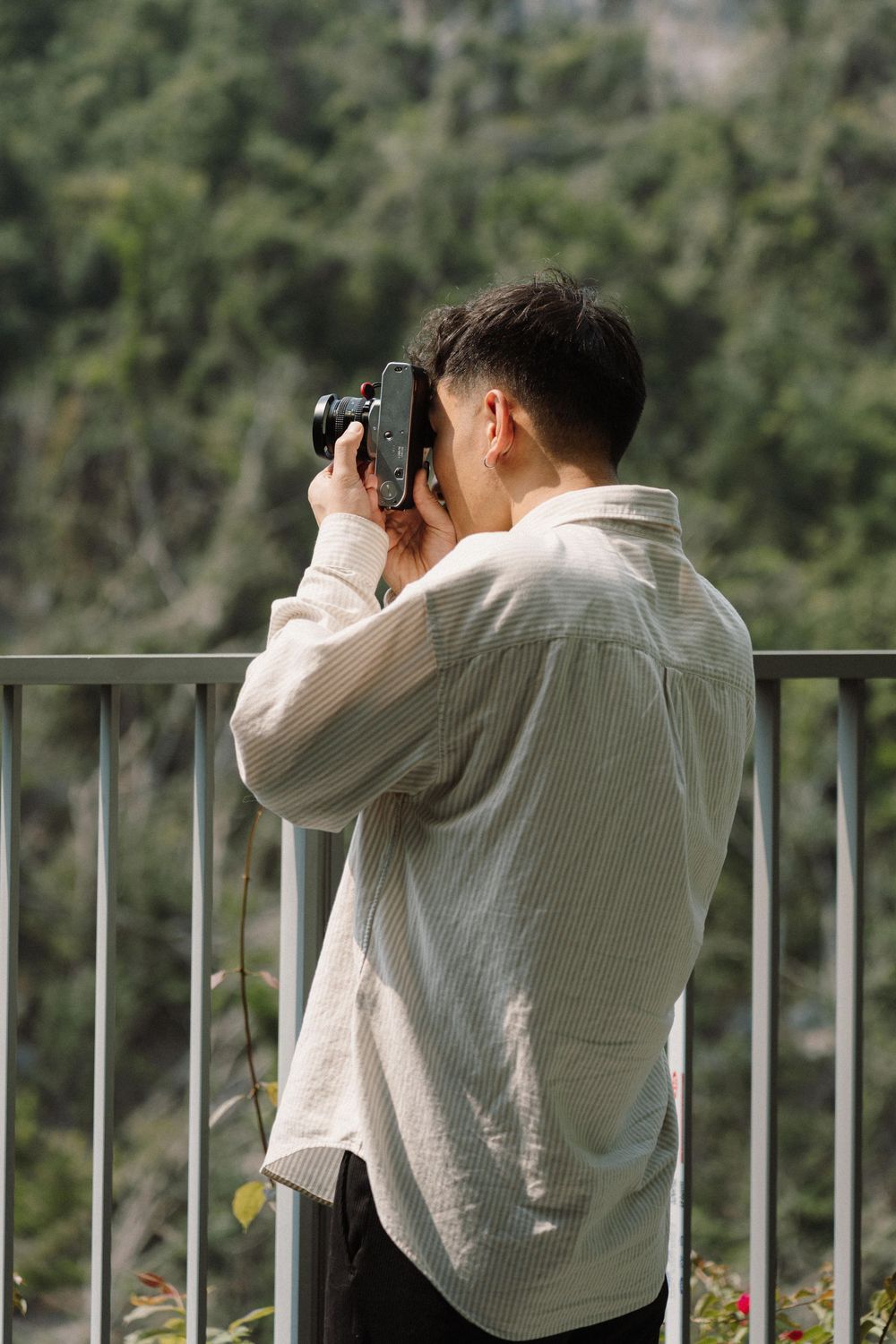 Photographer in white sweater taking pictures from a balcony overlooking nature.