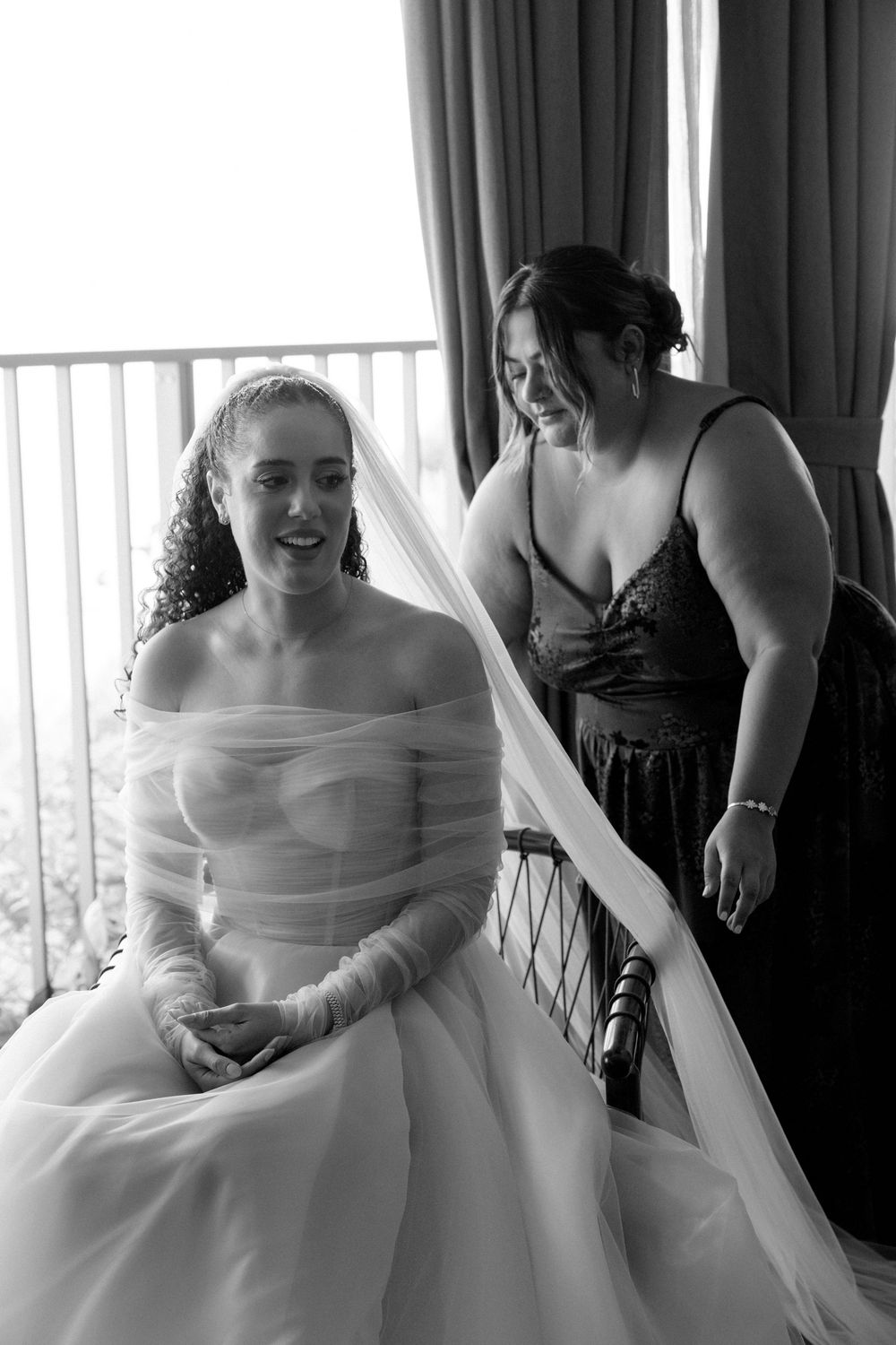 Bridal party sitting in a bright room smiling and laughing together during wedding day preparations.