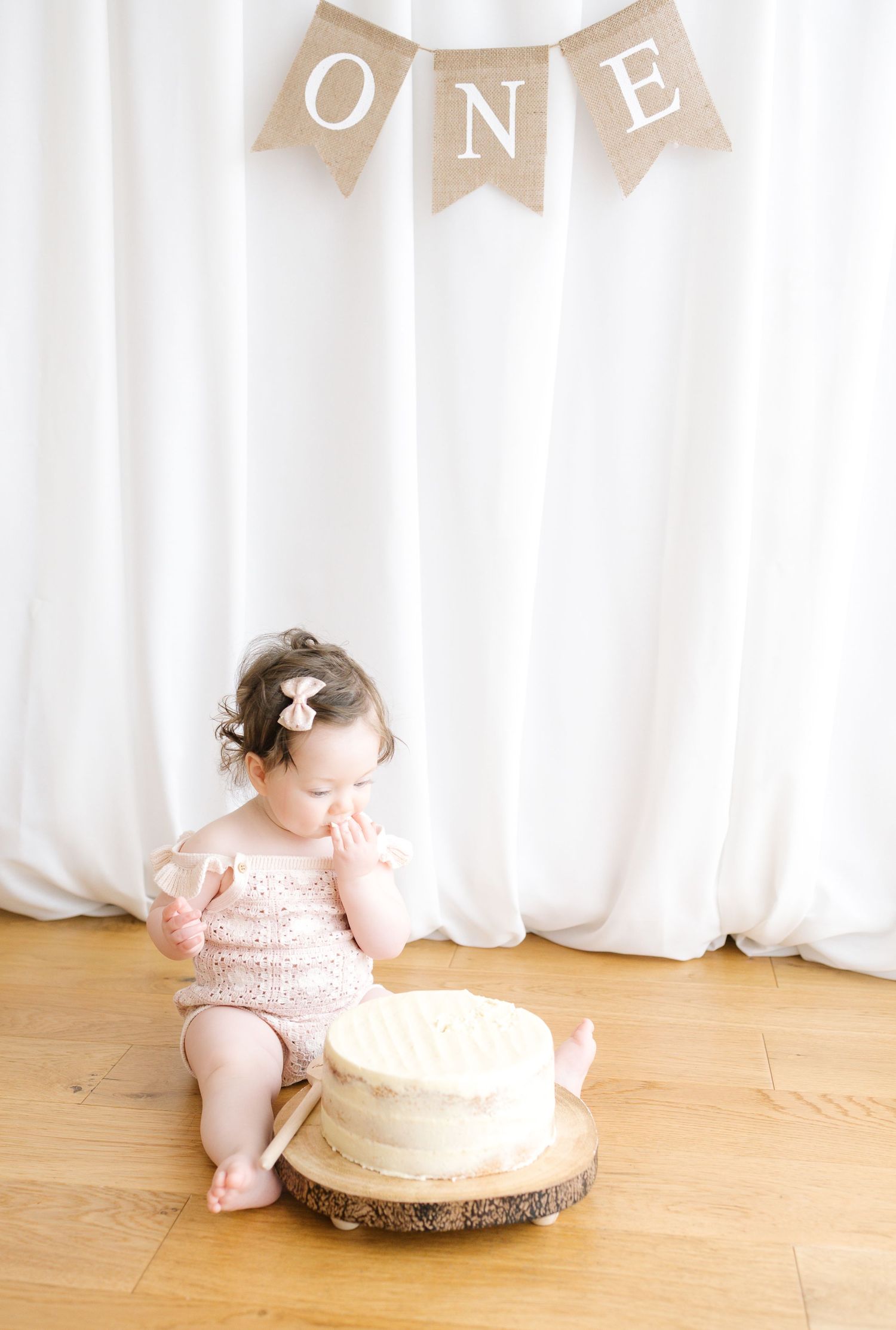 A tiny newborn baby wearing a white onesie lying peacefully on soft white bedding.