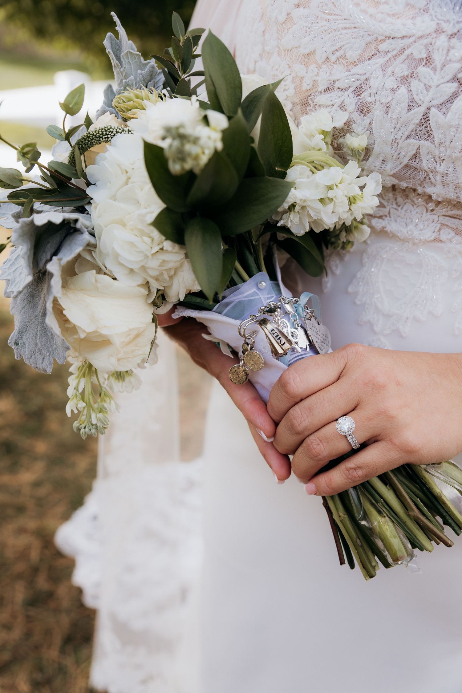 A wedding bouquet of white peonies and greenery held by hands wearing an engagement ring and wedding band.