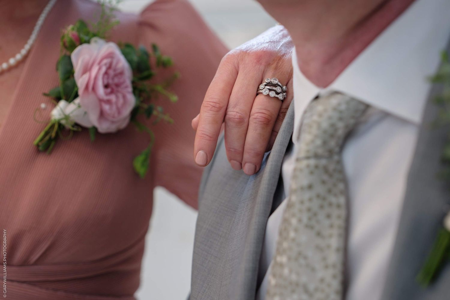Close up shot of two wedding bands resting on rustic wooden surface with pink flowers and greenery.