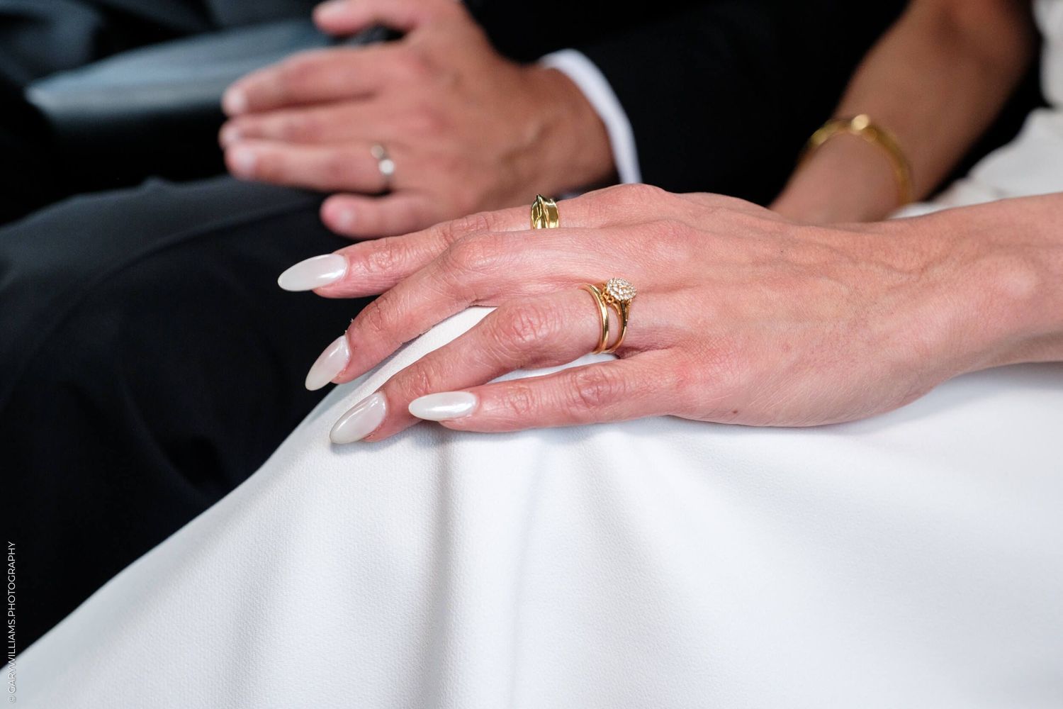 Gold wedding rings gleam against a white dress fabric during an intimate ceremony moment.
