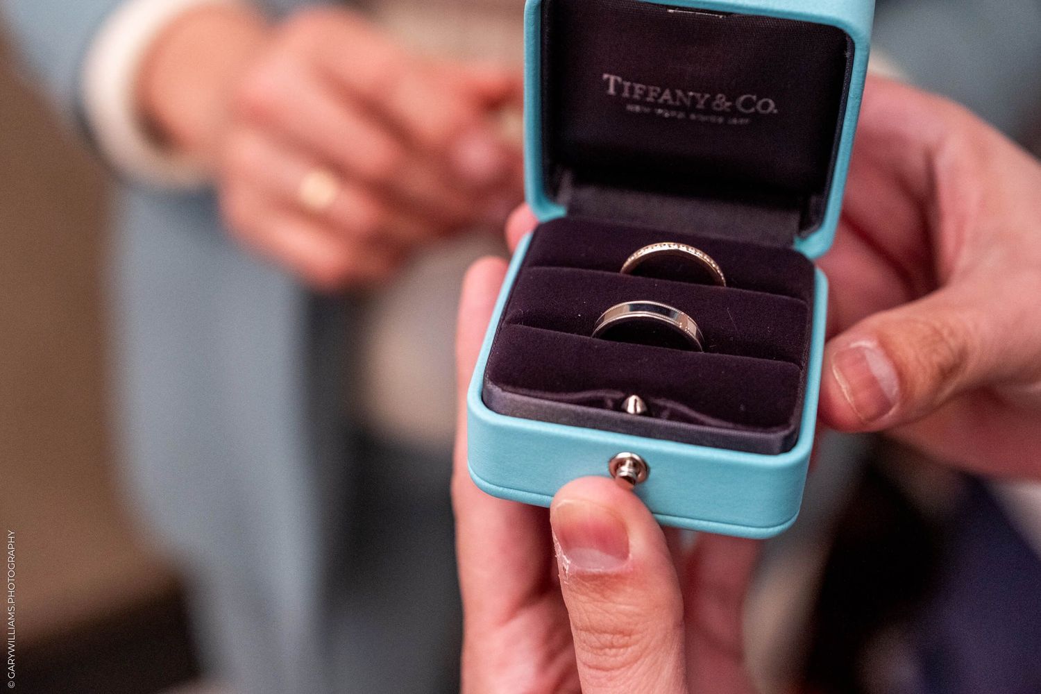Two wedding bands nestled in a Tiffany blue jewelry box held by gentle hands.