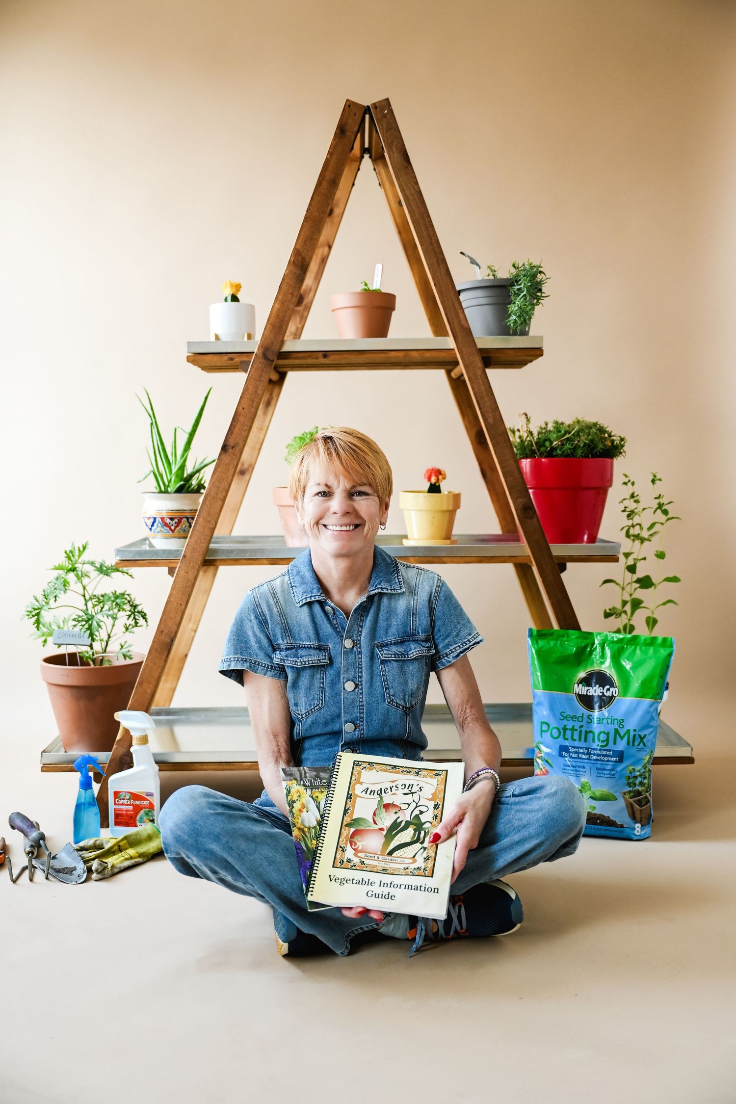 Person sitting cross-legged with colorful potted plants displayed on wooden ladder shelves.