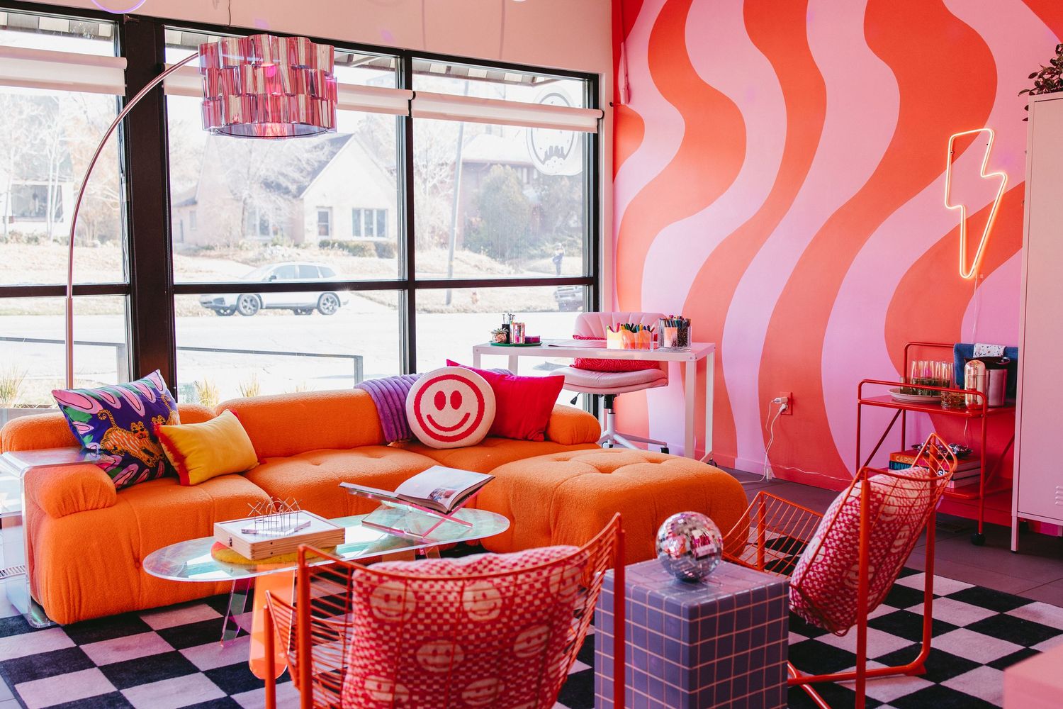 a fun lounge with an orange couch, a pink and red wavy mural, a black and white checkered rug, with smiley face decor