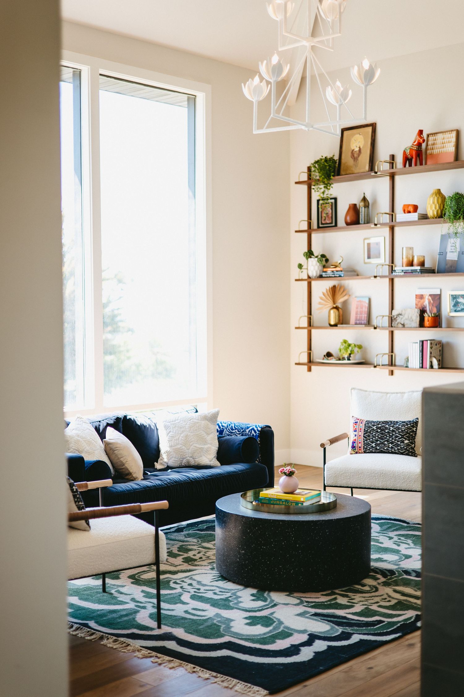 a bright, natural light room with a blue couch, a white modern arm chair, a circular stone coffee table, and decorated shelves
