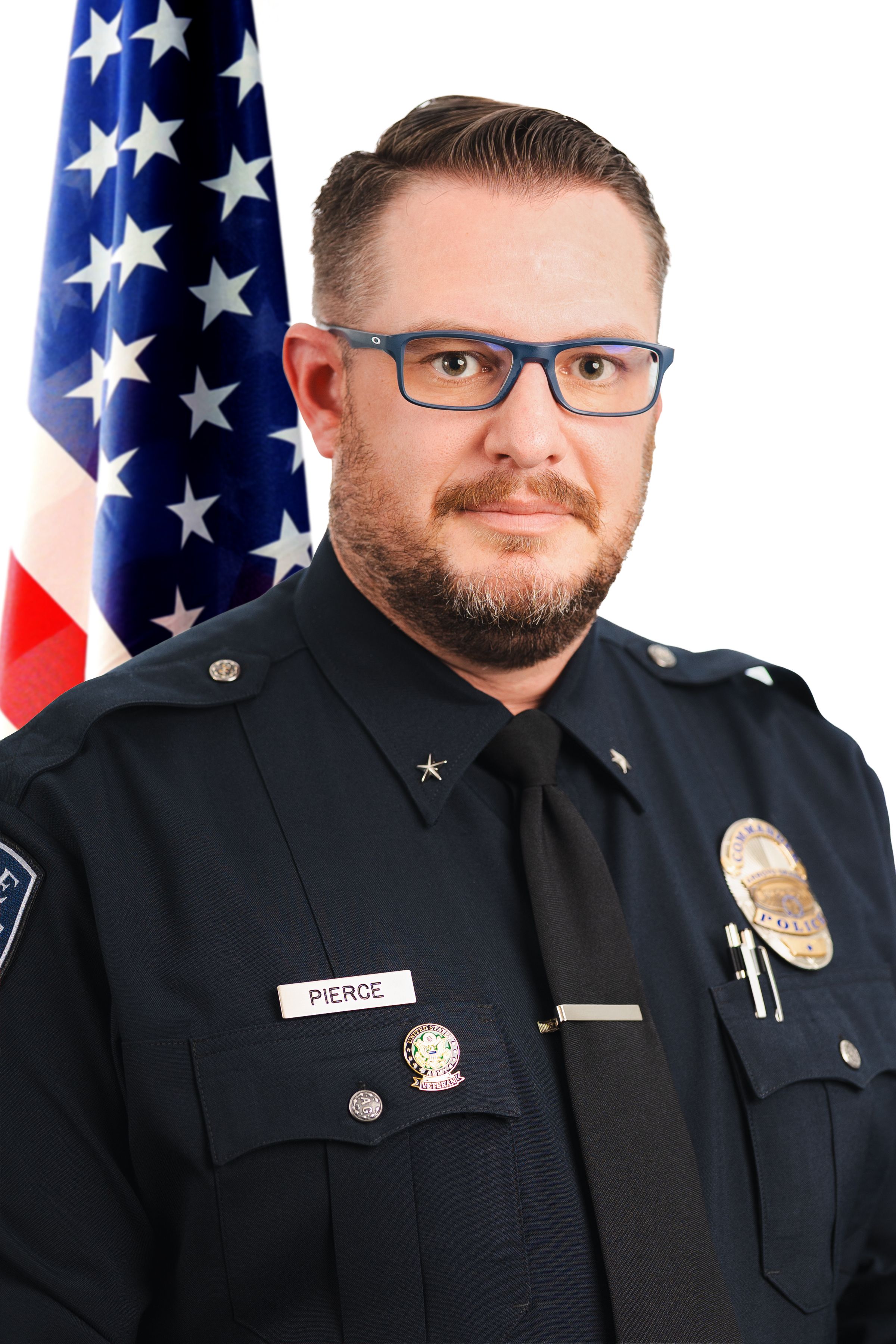 A police officer stares seriously at the camera for a headshot, with a big flag behind him.