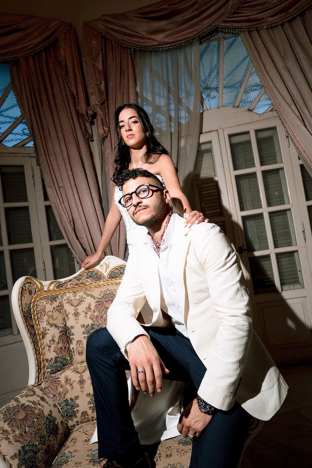 A romantic photoshoot series shows a couple in relaxed poses on an elegant vintage sofa with floral upholstery.