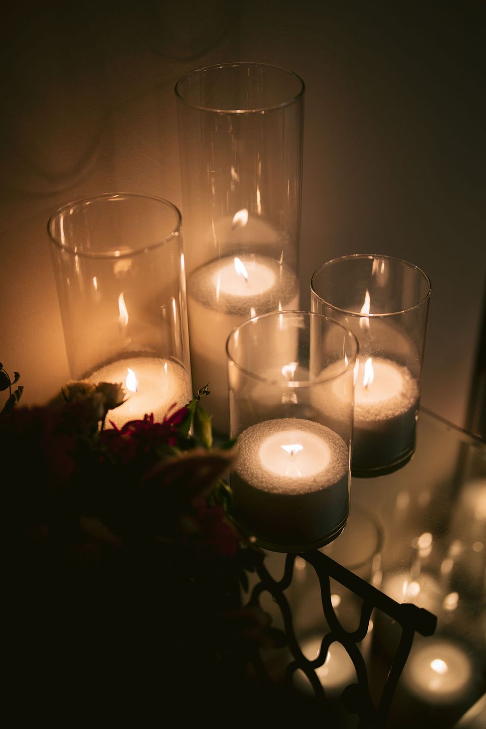 Four glass candle holders with glowing white candles creating a warm, romantic ambiance in dark lighting.