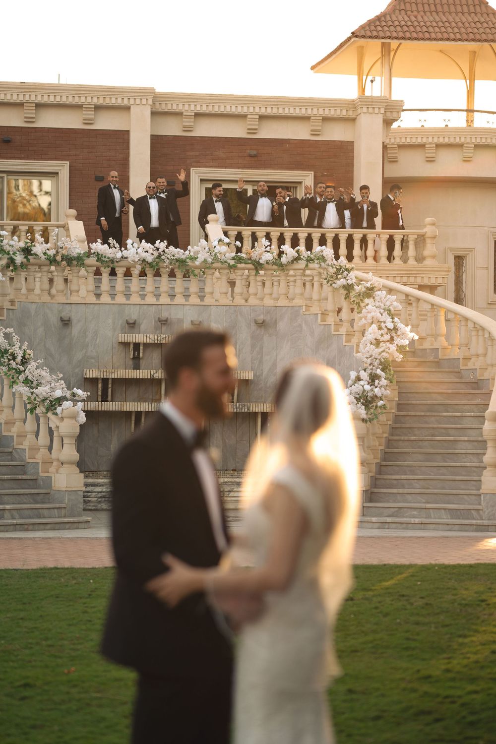 Wedding ceremony at elegant venue with stone staircase and gazebo during golden hour sunset.