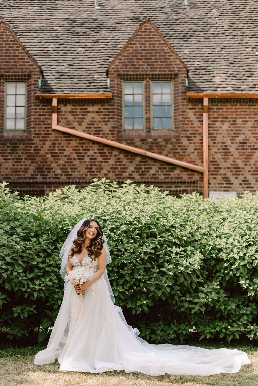 Elegant wedding photography scene against rustic brick building with lush greenery.