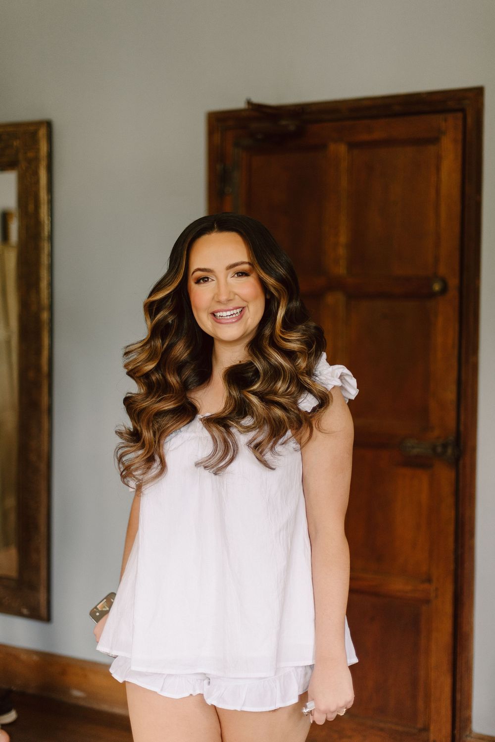 Woman wearing a white loungewear set with flowing curled hair preparing for a special day.