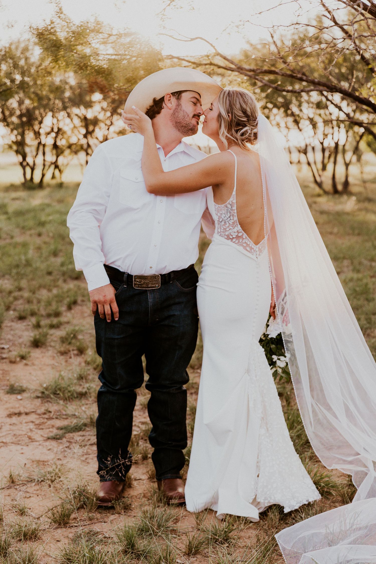 Newly weds kissing in the trees with the sun streaming in.