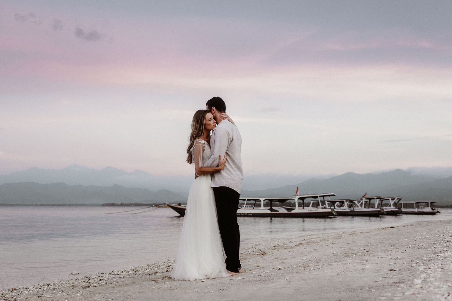 Close-up view of two people holding hands against a misty natural background at sunset.