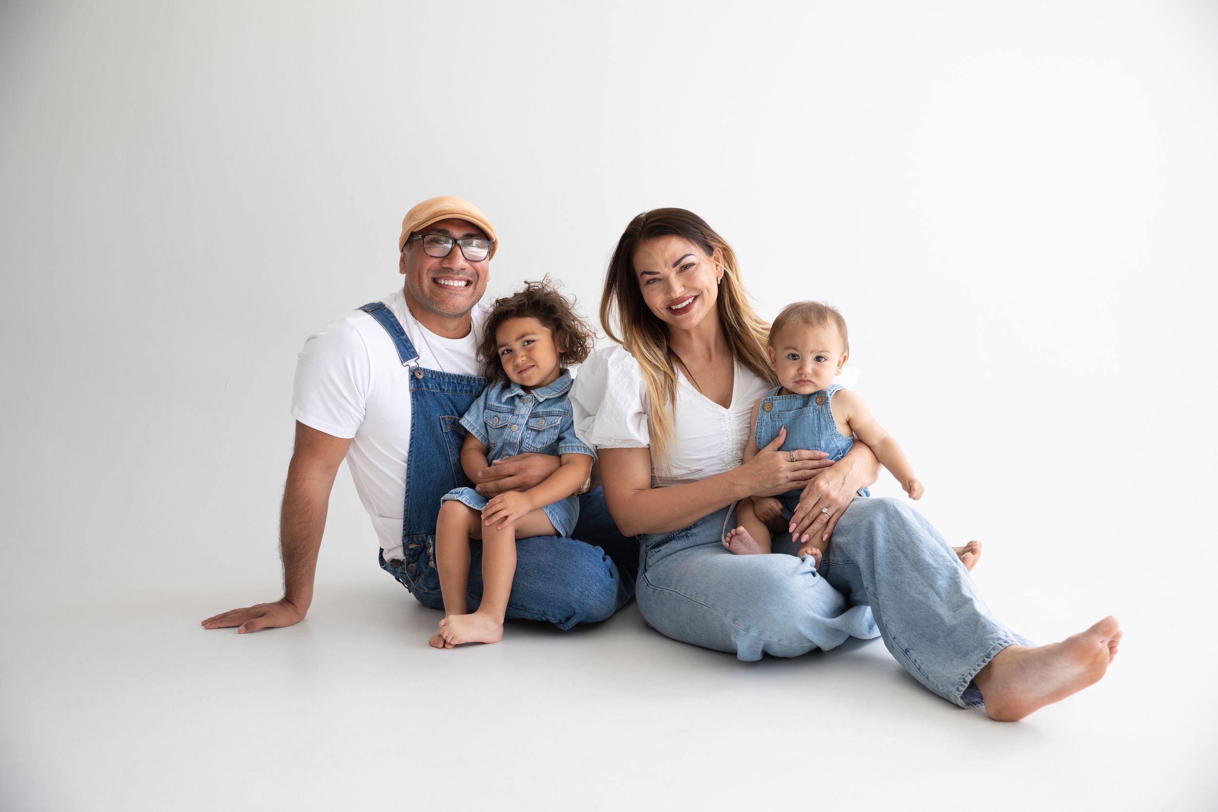 A family in matching white shirts and jeans sits together on a white background.