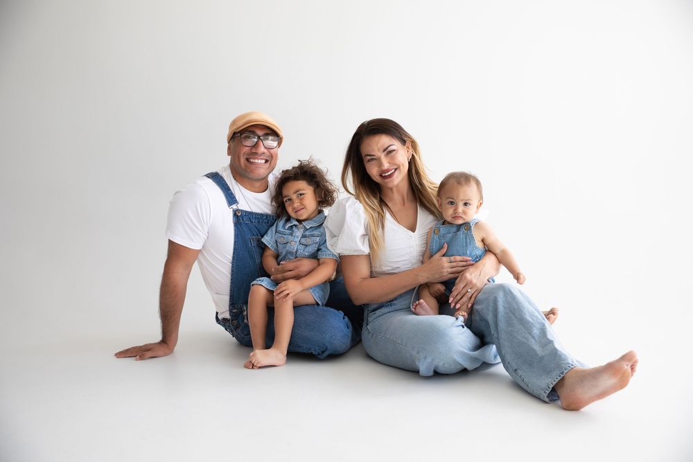 A family in matching white shirts and jeans sits together on a white background.