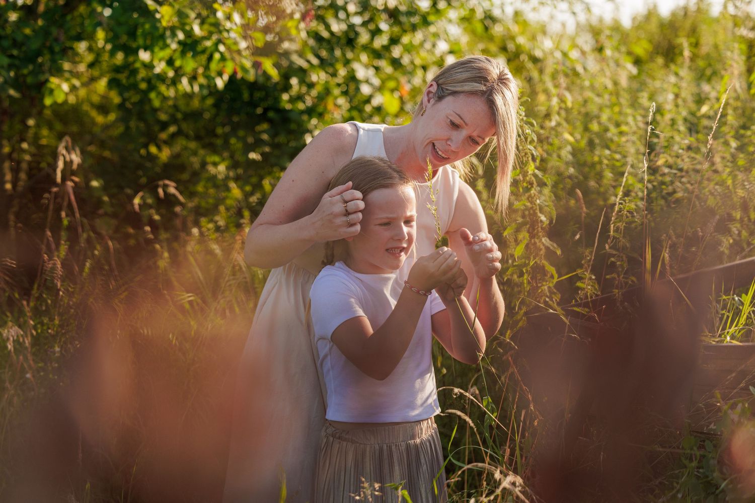 Two people embrace during a sunny outdoor golden hour photoshoot in a grassy meadow at sunset.