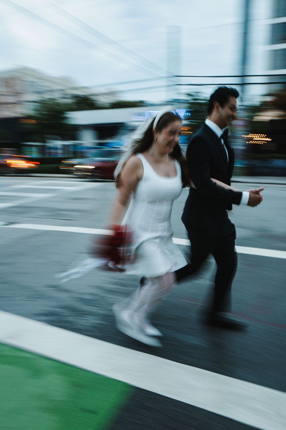 A bride in a white dress and groom in black suit running across a street in motion blur on their wedding day.