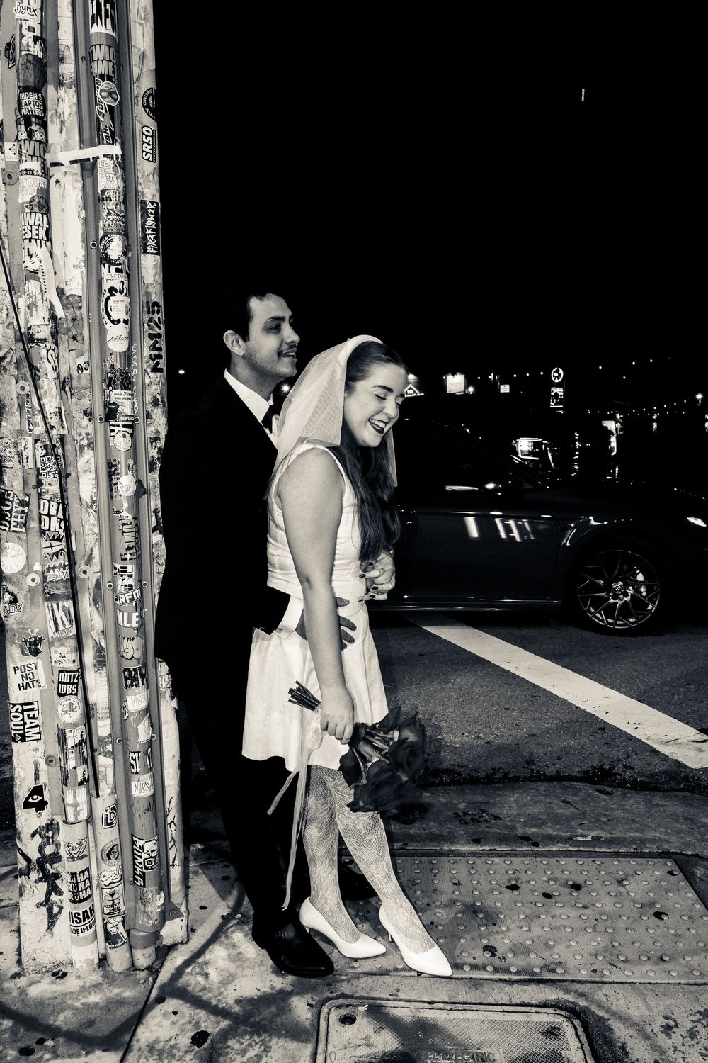 Black and white vintage style photo of a couple dressed in formal attire standing on a city street at night.