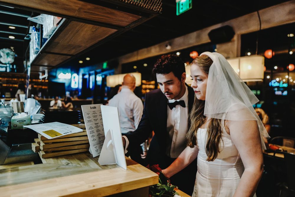 A person in a white wedding dress walks down a long dark hallway with glowing lights on the ceiling.